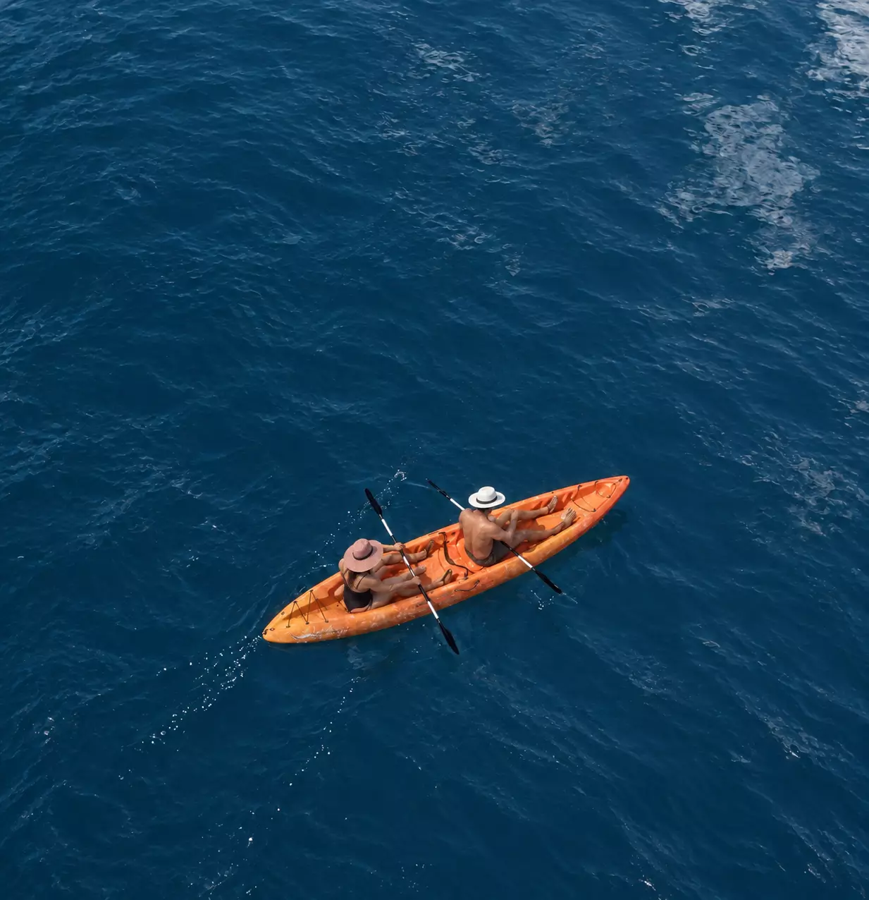 Vista cenital de un kayak naranja con dos personas sobre el mar azul.