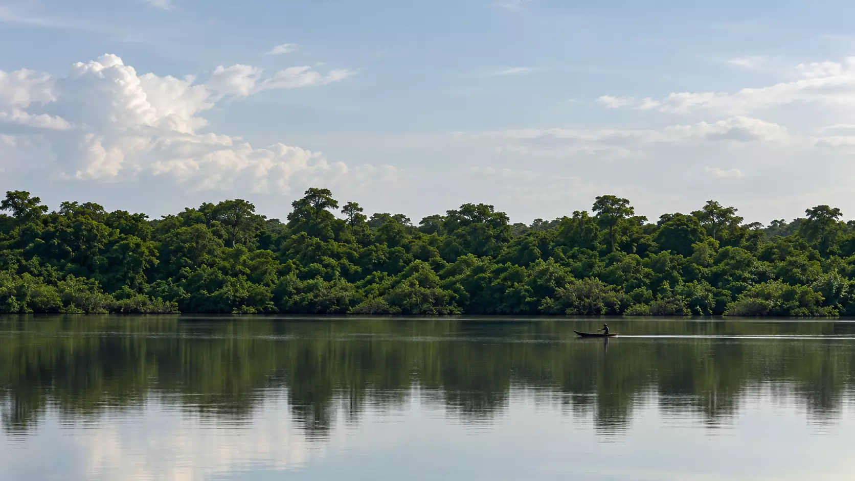 La laguna en calma con una canoa a lo lejos y la vegetación reflejada en el agua.